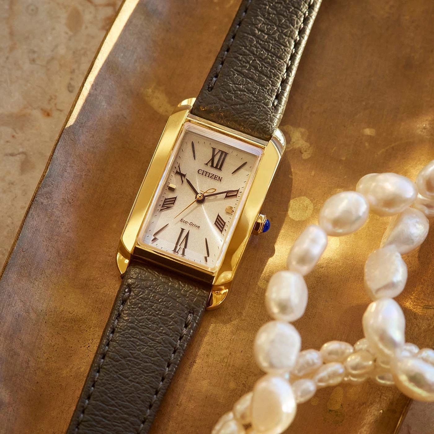 Citizen watch with a gold case and a leather strap, next to pearls.