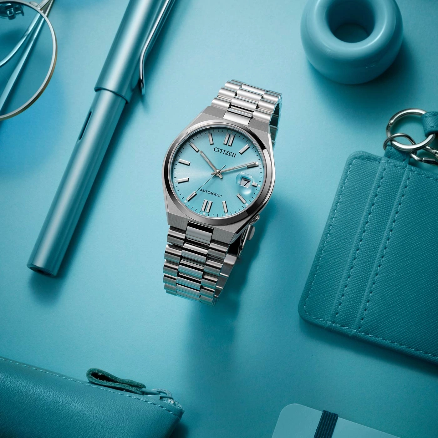 Citizen watch, pen, glasses, and accessories on a blue surface.