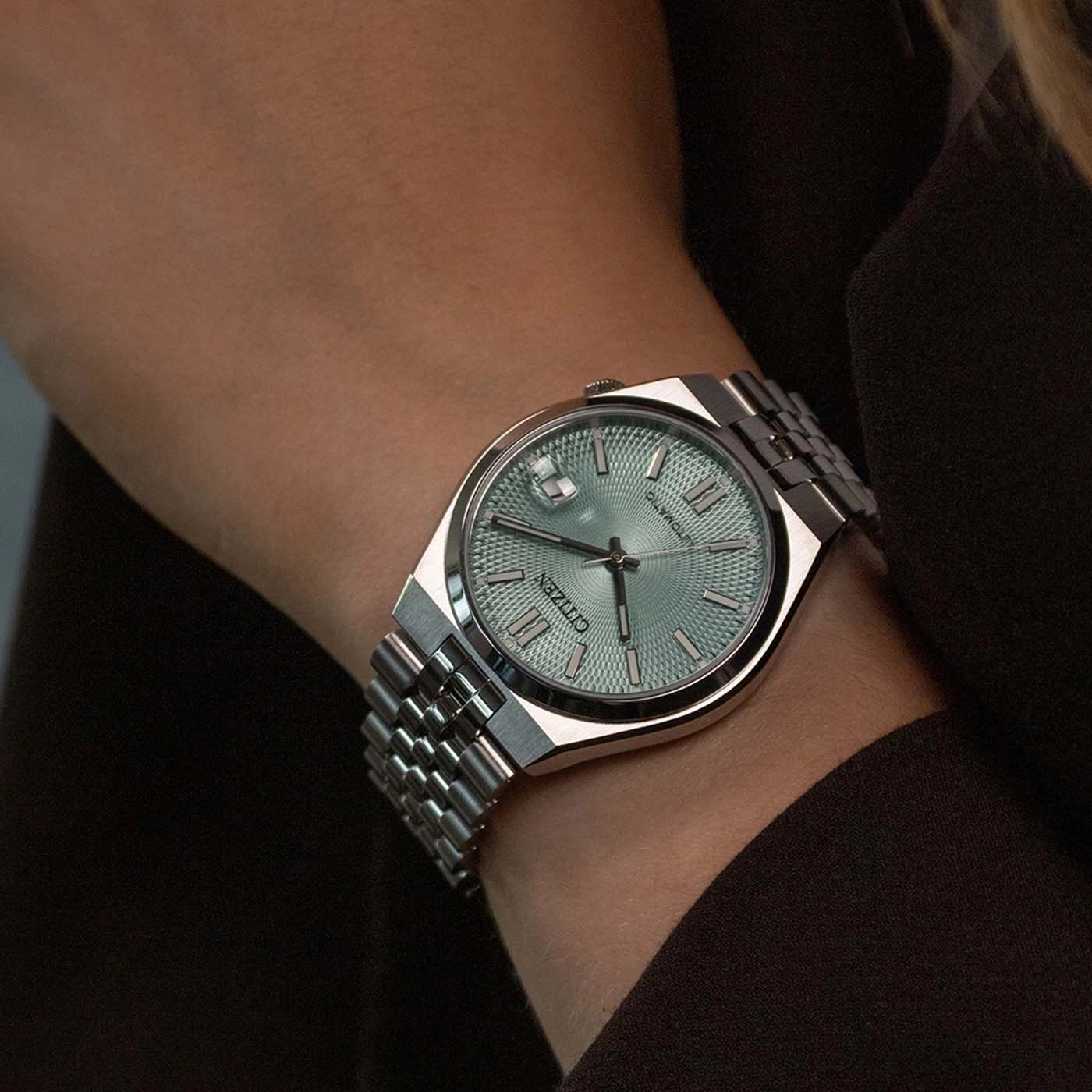 A person wearing a Citizen watch with a green dial on their wrist.