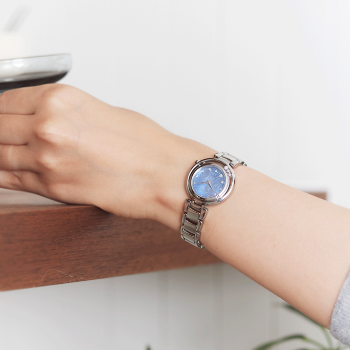 A woman's wrist with a silver watch, blue face, and snowflake design.