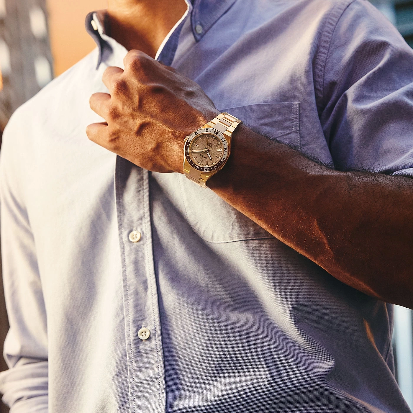 Man wearing a gold watch, buttoning his light blue shirt.