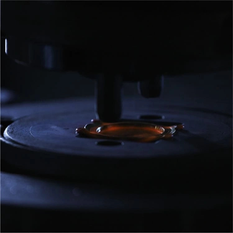 Close-up of a dark machine with a drop of orange liquid on a plate.