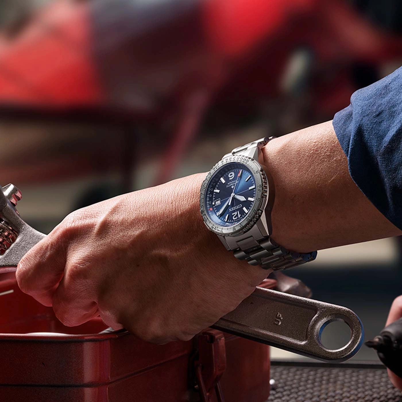 Close-up of a person wearing a watch and holding a wrench, working on a car.