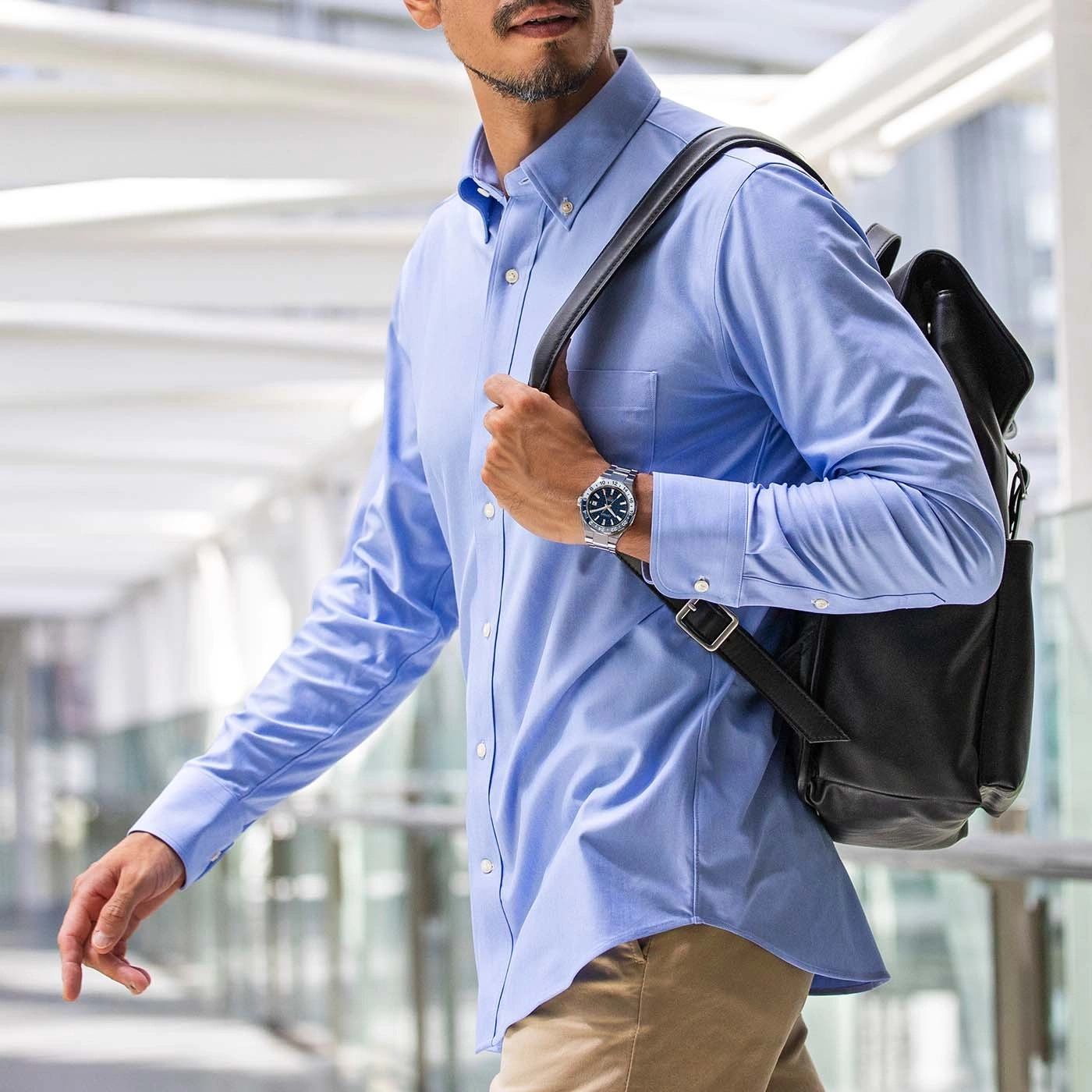 Man in blue shirt with watch and backpack walking in a building