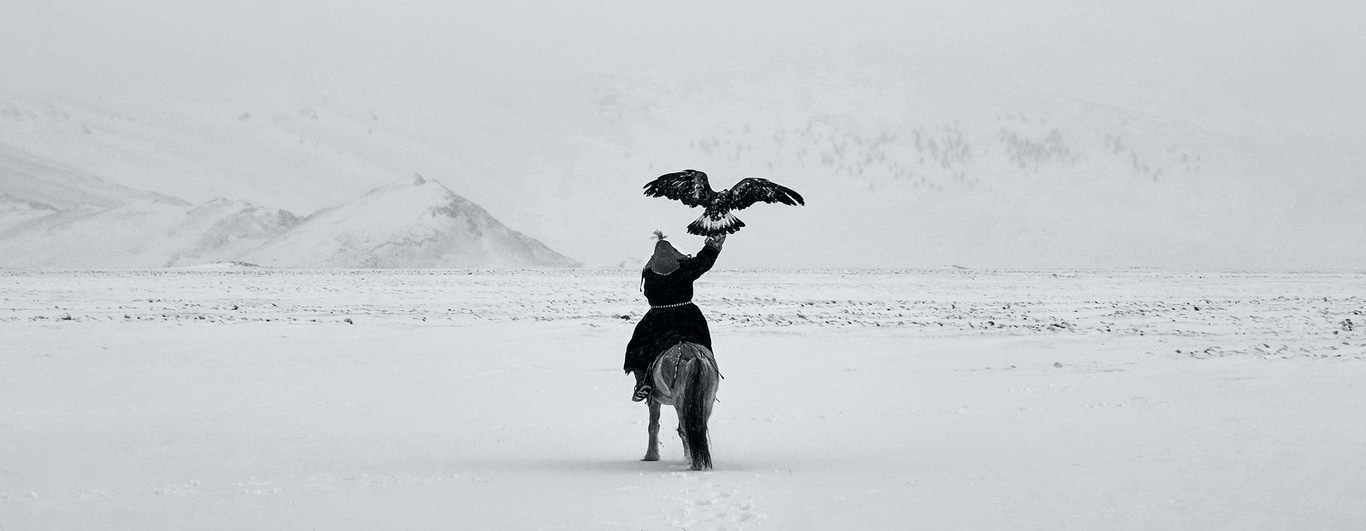 Eine Person auf einem Pferd mit einem Adler in einer verschneiten Landschaft.