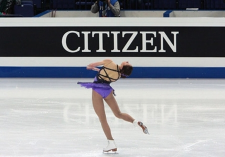 Figure skater in a purple dress performing a spin on the ice.
