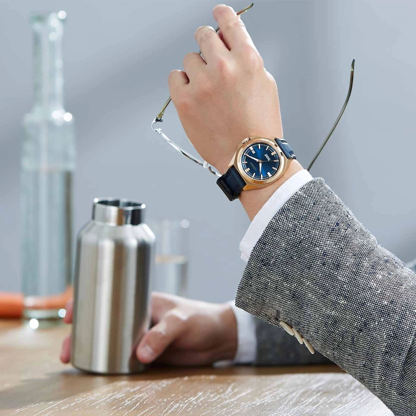 Man wearing a watch, holding glasses and a water bottle, business attire