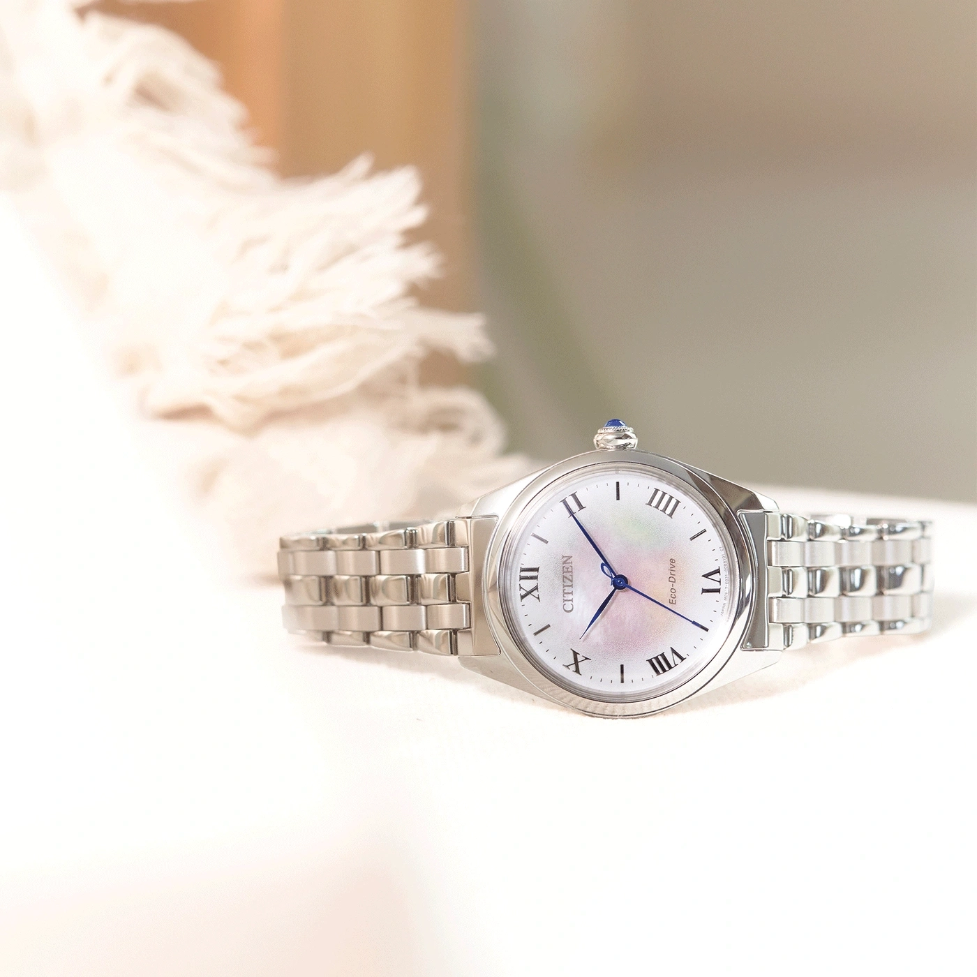 Citizen watch with a white face and silver band on a white surface.