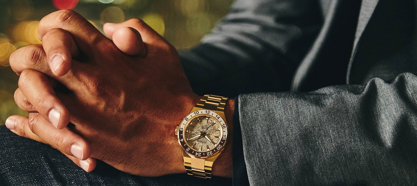 Man wearing a gold watch, hands clasped, suit jacket, bokeh background.