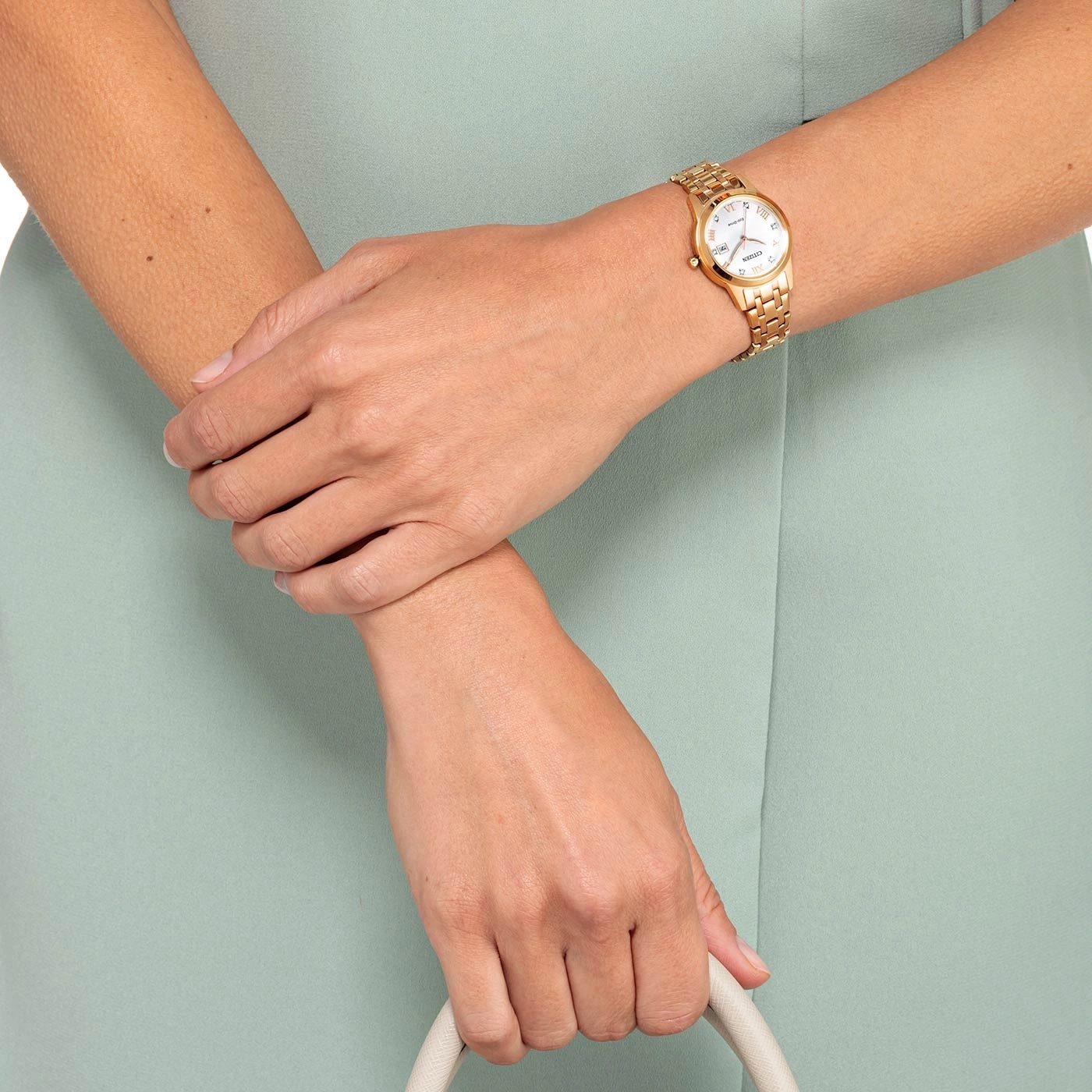 Woman wearing a gold watch, holding a purse, light green dress