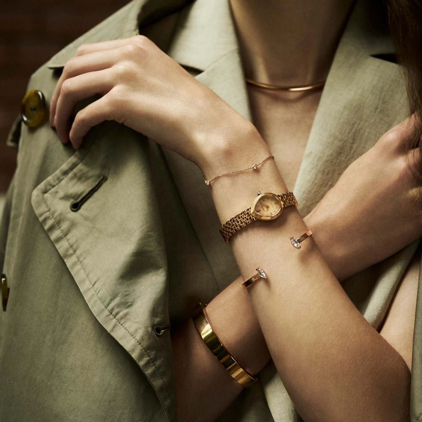 Close-up of a woman's arms adorned with gold jewelry, including a watch and bracelets.