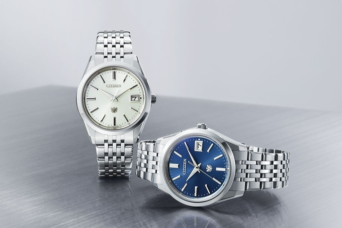 Two Citizen watches with silver straps and different colored faces.