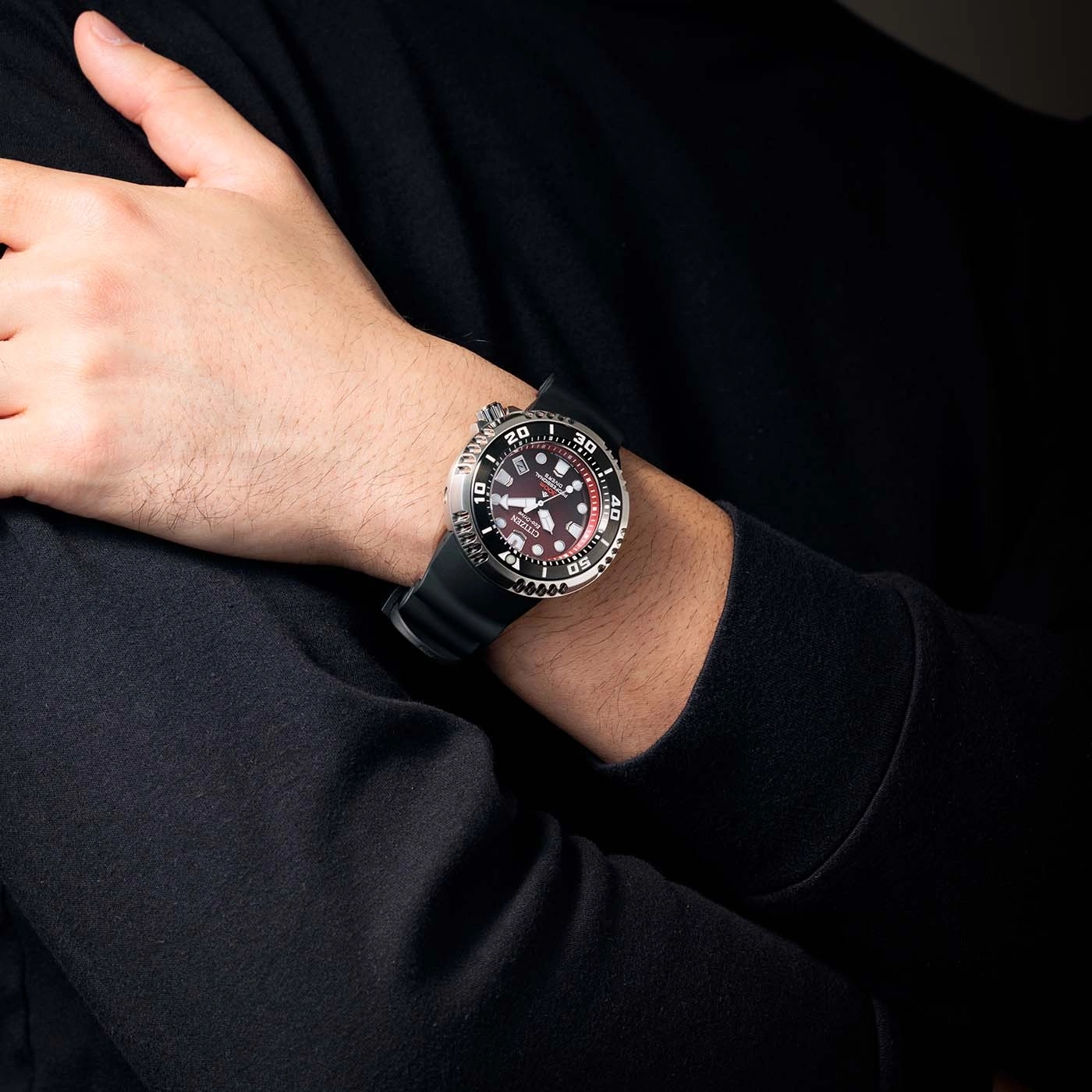 Man wearing a Citizen watch with a black strap and a red dial.