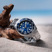 Citizen watch on sand with blue dial and ocean background