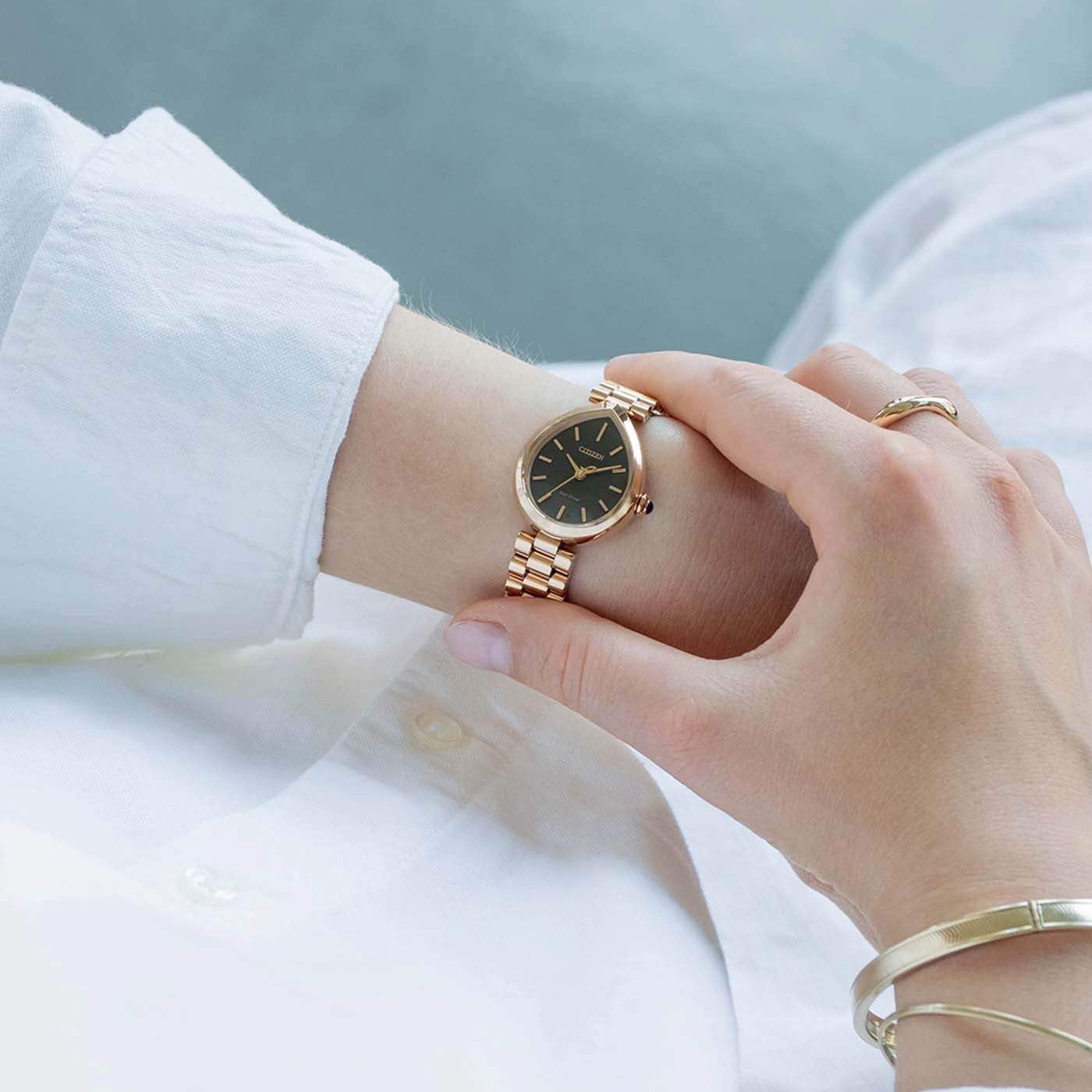 A woman wearing a gold watch and bracelet, touching her face.