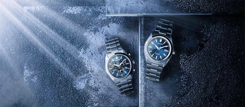 Two Citizen watches with blue dials on a textured surface.