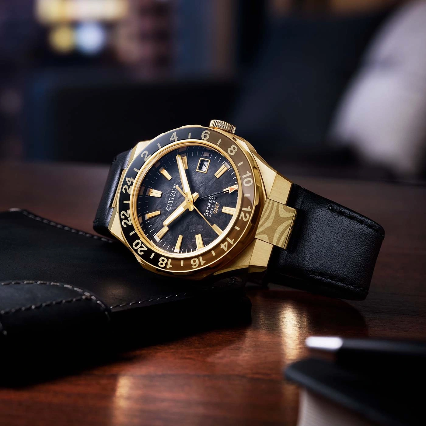 A gold Citizen GMT watch with a black dial and leather strap.