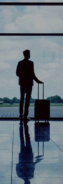 Man with suitcase at airport window, waiting for flight, silhouette