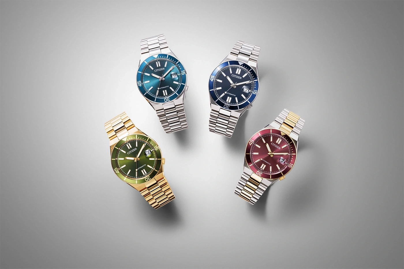 Four Citizen watches with different colored dials and metal bands on a gray background.