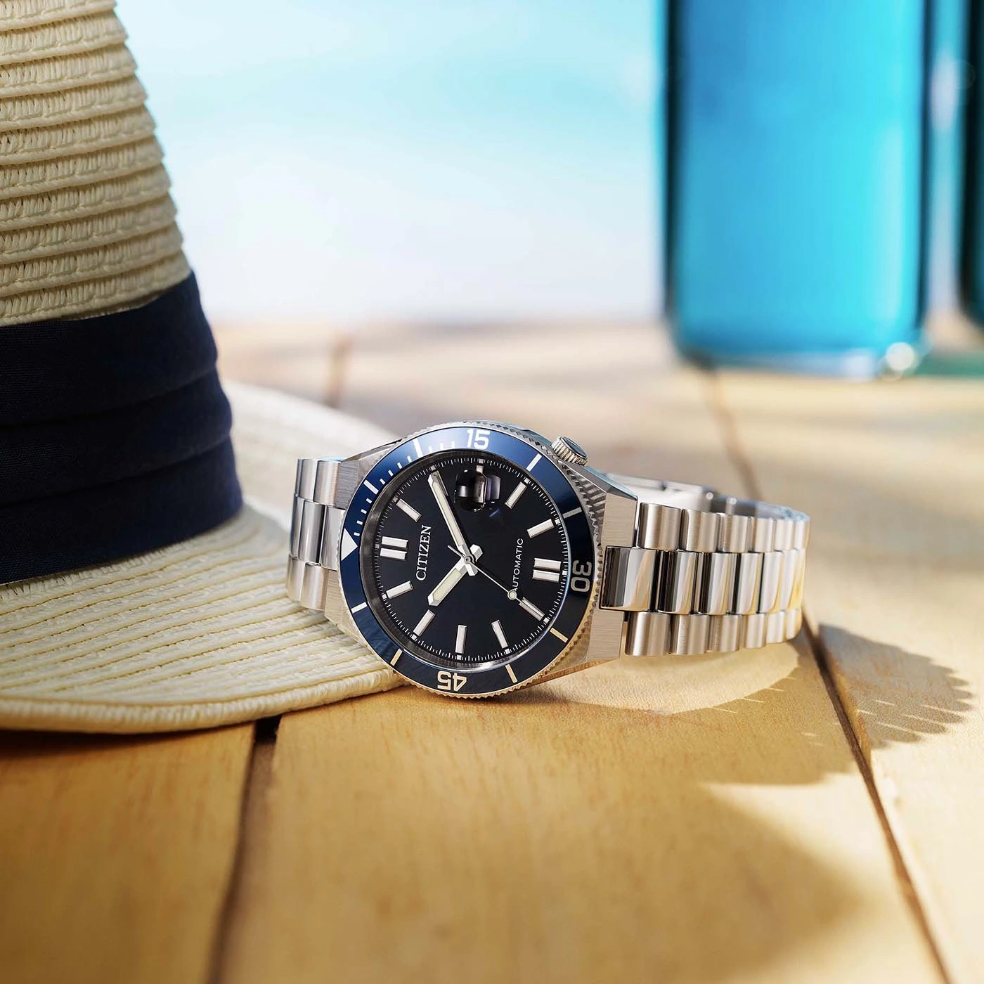 A Citizen watch on a wooden table with a hat and drinks.
