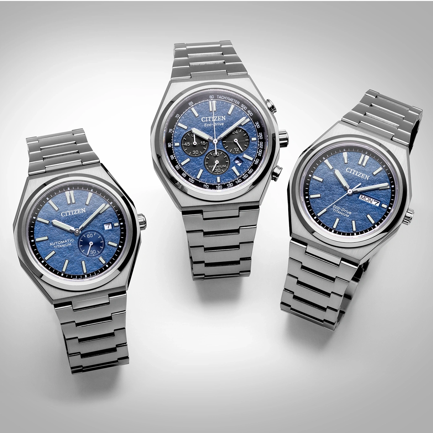 Three Citizen watches with blue faces and titanium bands on a white surface.