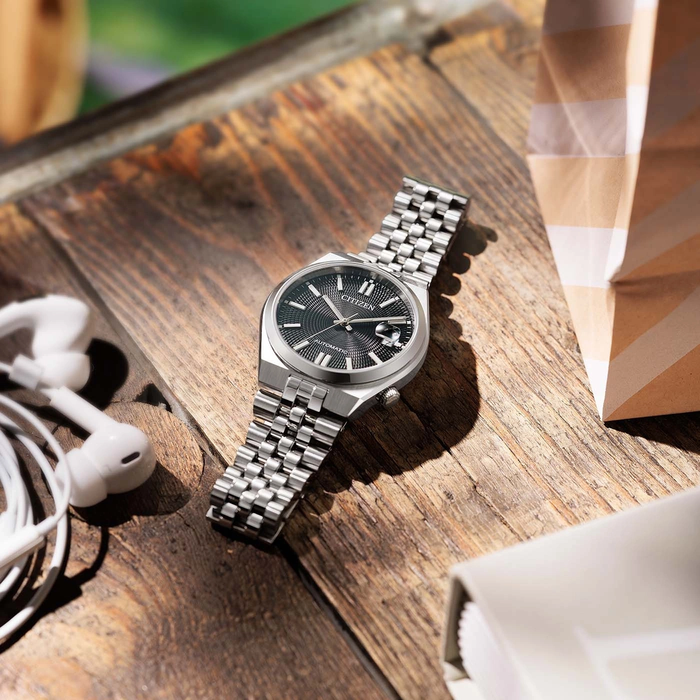A close-up shot of a Citizen watch on a wooden table with earbuds.