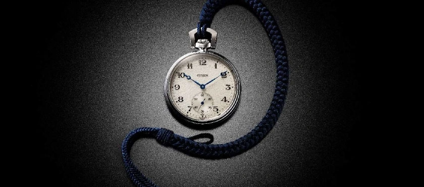 Pocket watch with blue hands and a blue cord on a dark background.