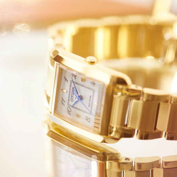 Close-up of a gold Citizen watch with a rectangular face and blue hands.