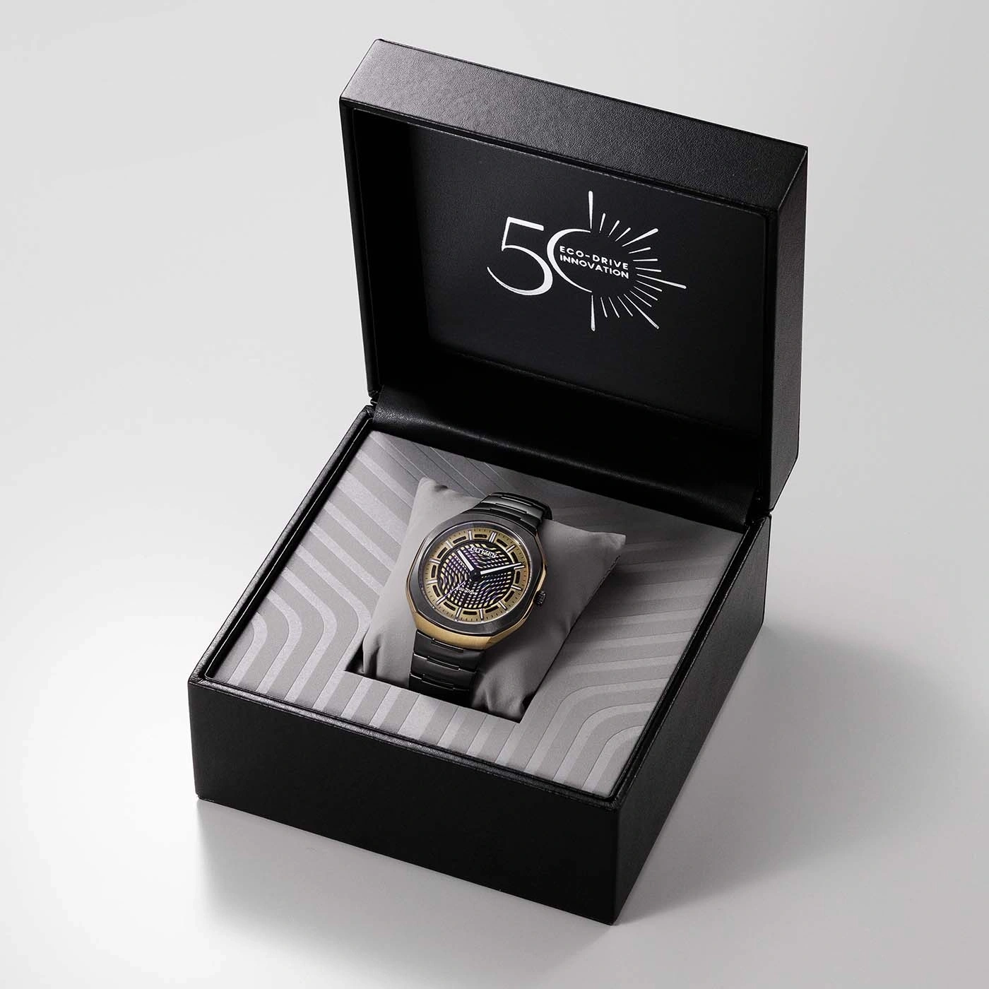 A black and gold watch in an open box with "50 ECO-DRIVE INNOVATION" printed inside the lid.