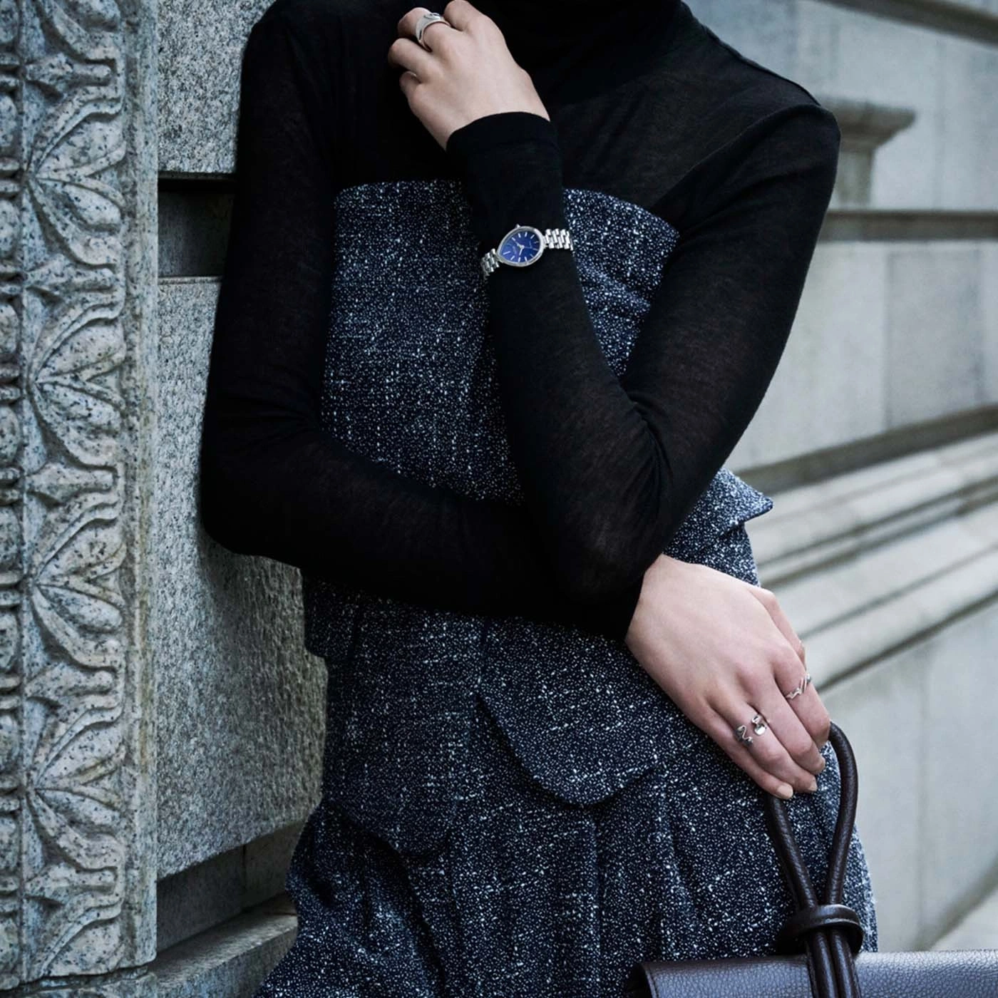 Woman in black turtleneck and textured dress wearing a watch and rings.