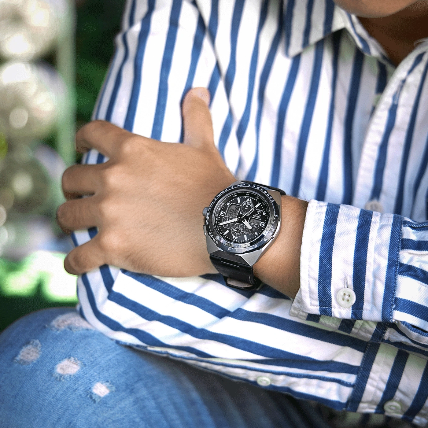 Man wearing a watch, blue and white striped shirt, and ripped jeans.
