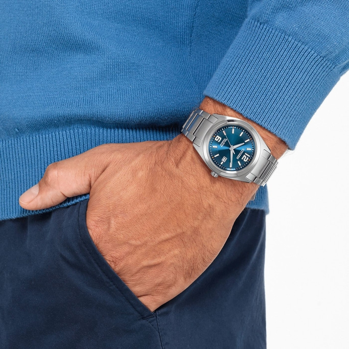 Man wearing a blue watch and sweater, hand in pocket.