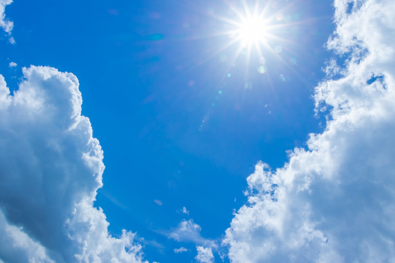 Bright sun shining in a clear blue sky with fluffy white clouds.