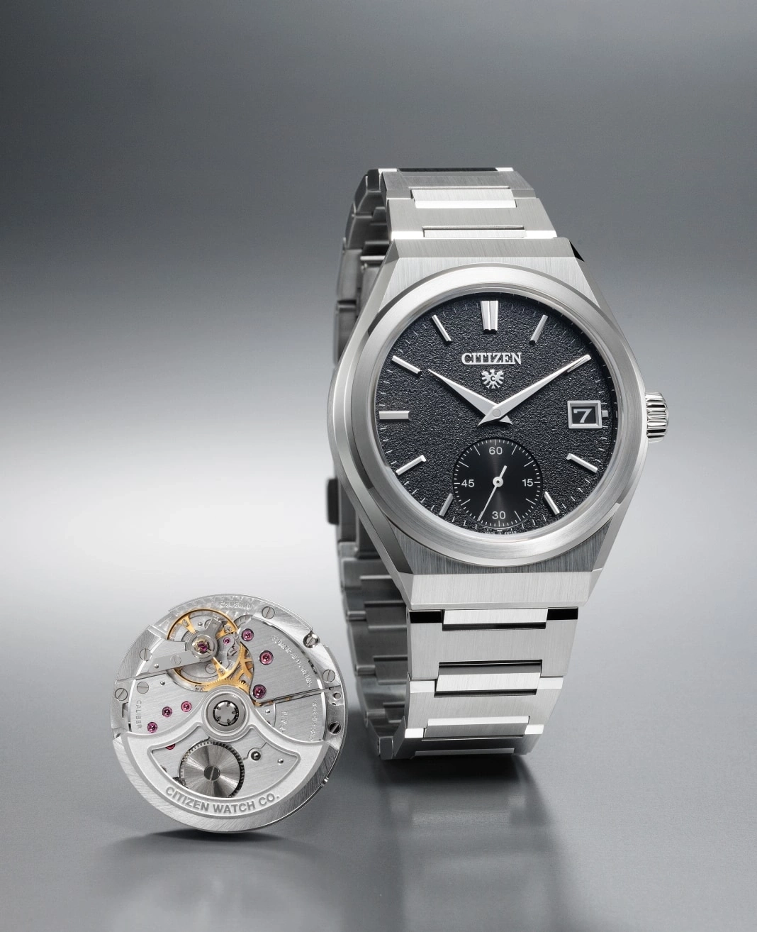 Citizen watch with exposed mechanism and stainless steel bracelet on a gray surface.