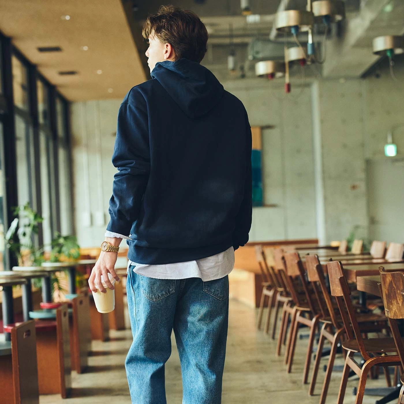 Man in hoodie and jeans holding a coffee cup in a cafe