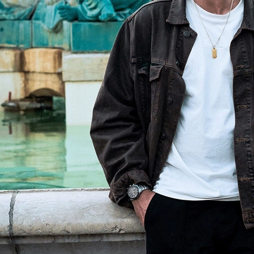 Man in brown jacket and white shirt, watch, leaning on a wall