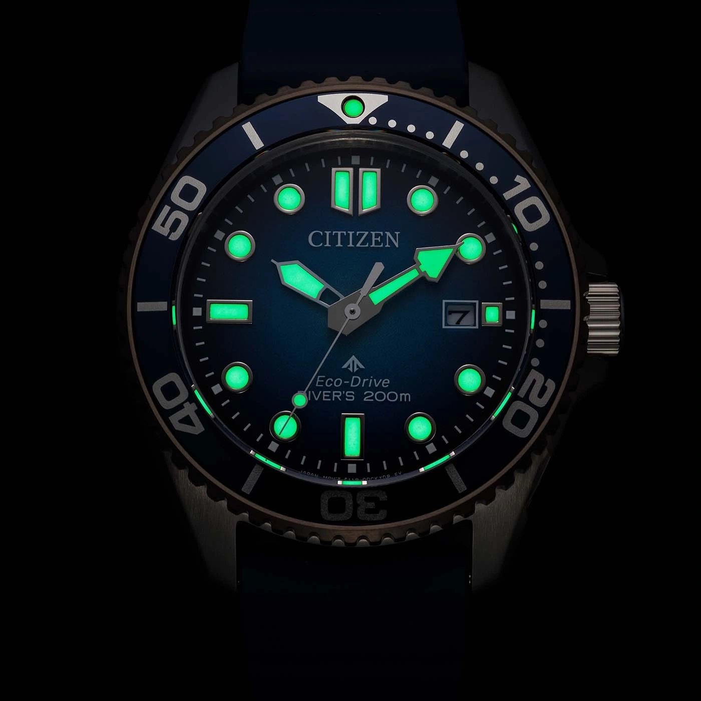 A close-up of a luminous blue Citizen Eco-Drive diver's watch at night, showing glowing markers and hands.