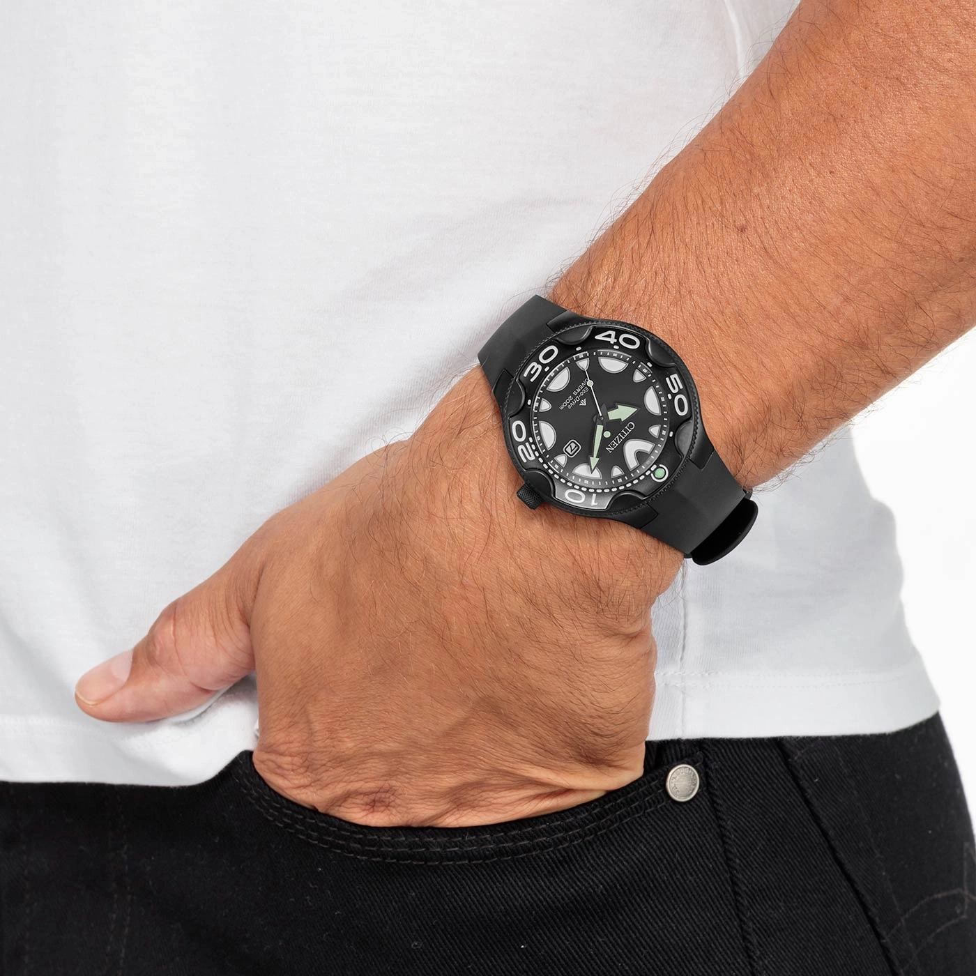 Man wearing a black watch, white shirt, and black jeans with his hand in his pocket.
