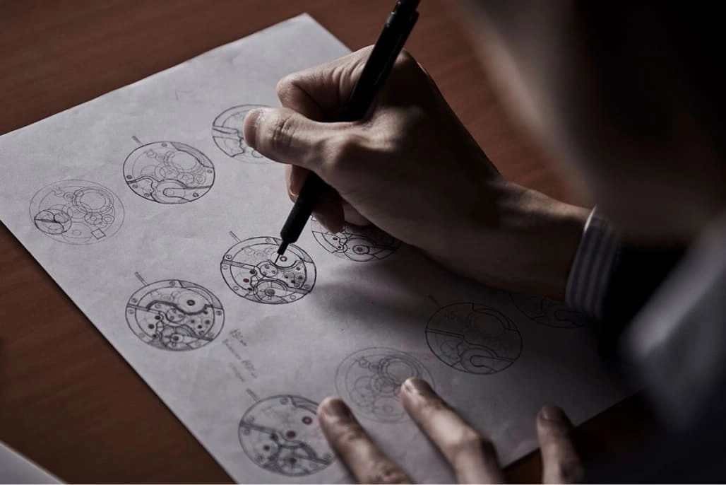 A person sketching watch designs on paper with a pen, close-up shot.