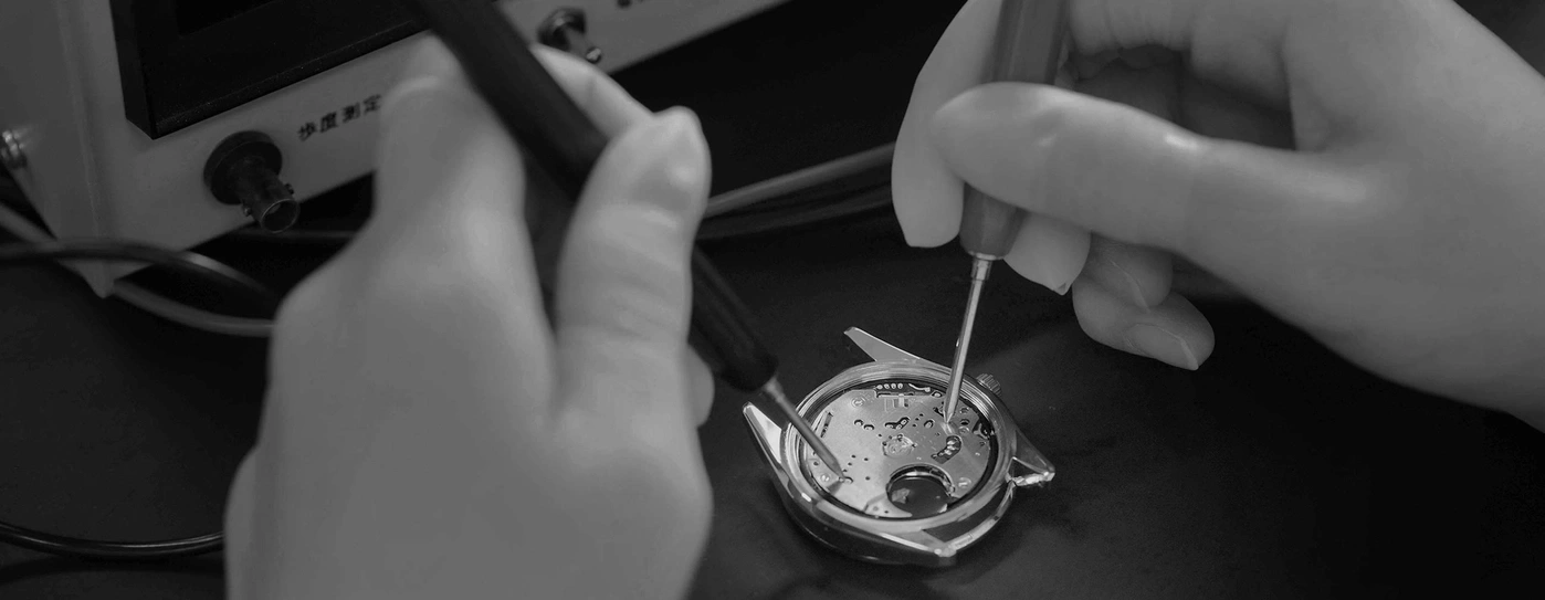Watch repair with tools and hands, close-up, black and white, precision work.