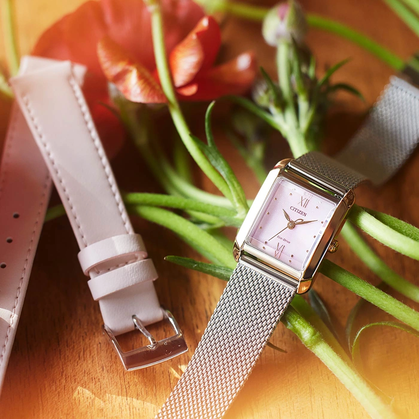 Citizen watch with pink face and mesh strap, with a spare leather strap and flowers.