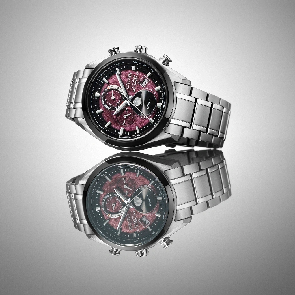 Citizen watch with a red face and titanium band, reflected on a surface.