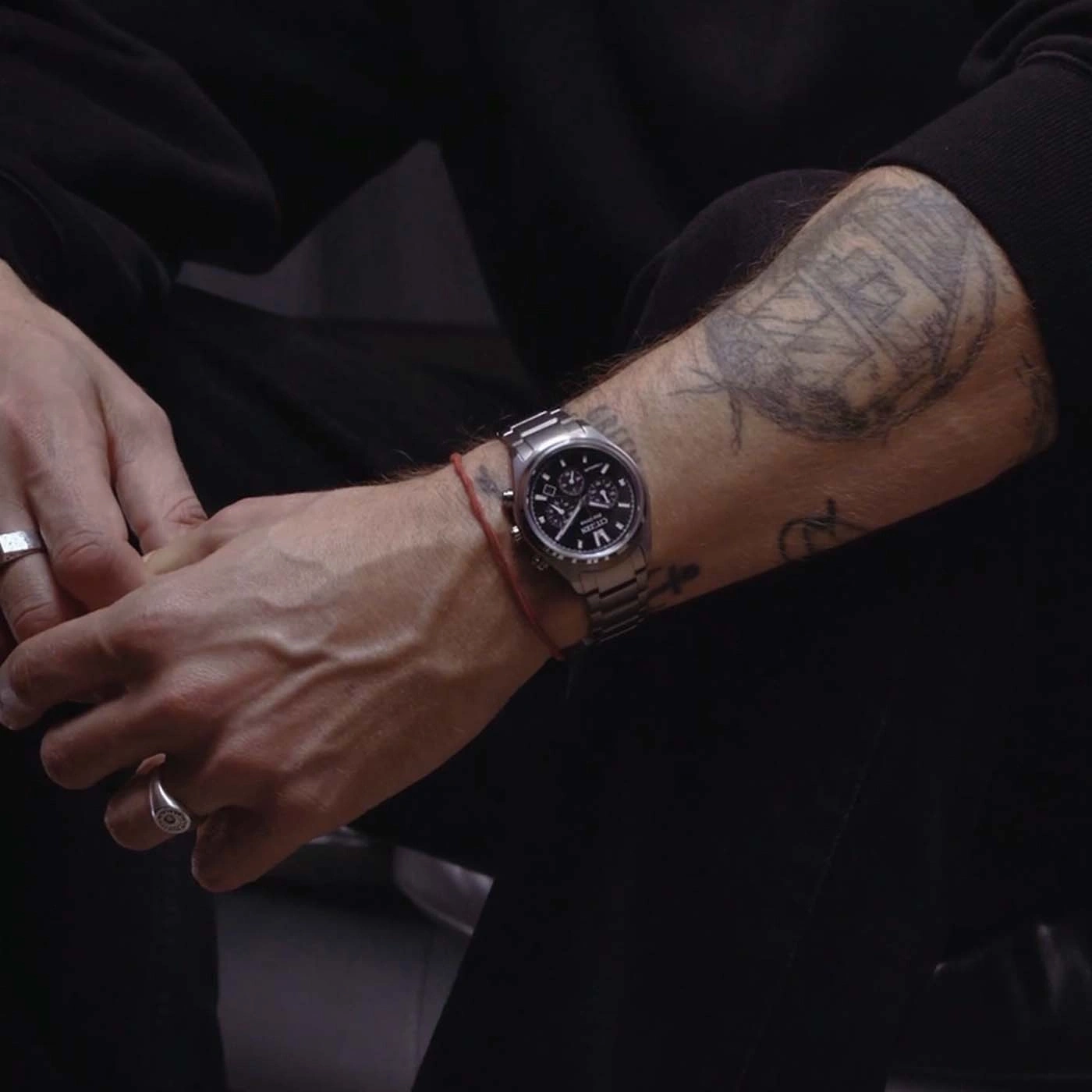 Close-up of a man's tattooed arm wearing a watch and rings.