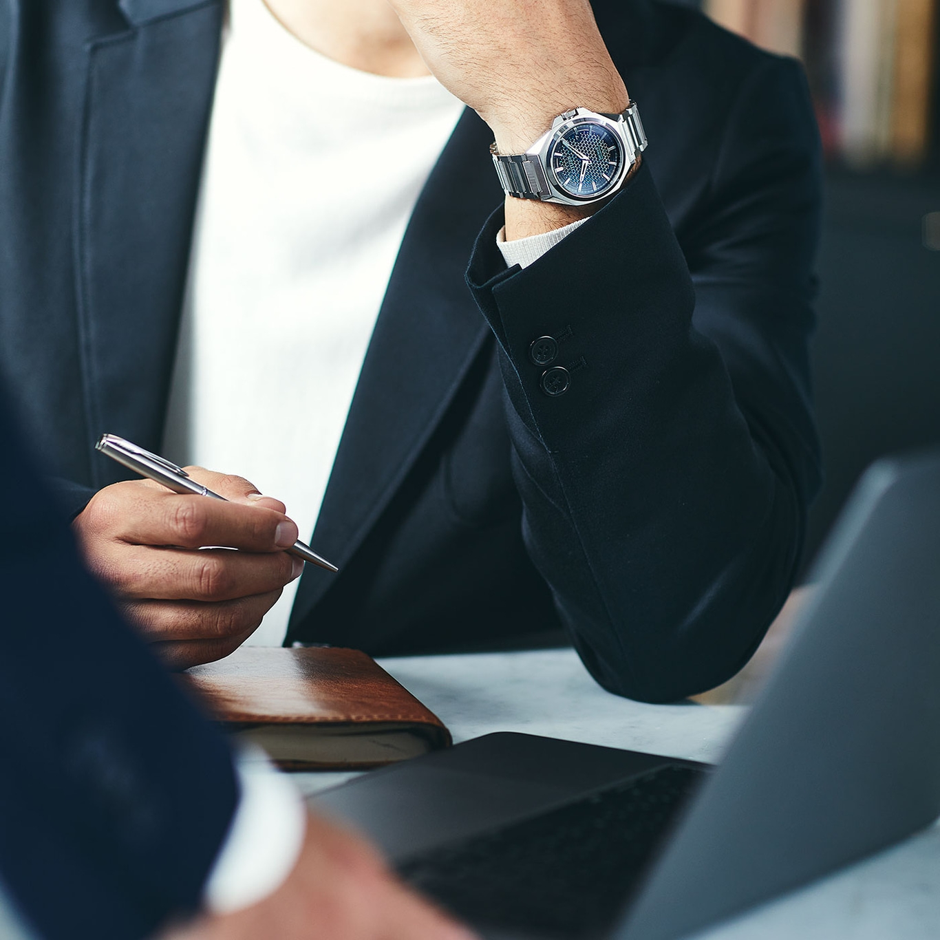 Man in suit with watch and pen, working on laptop, business meeting.