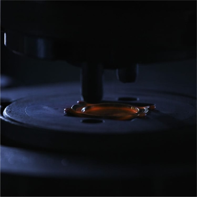 Close-up of a dark machine with a drop of orange liquid on a plate.