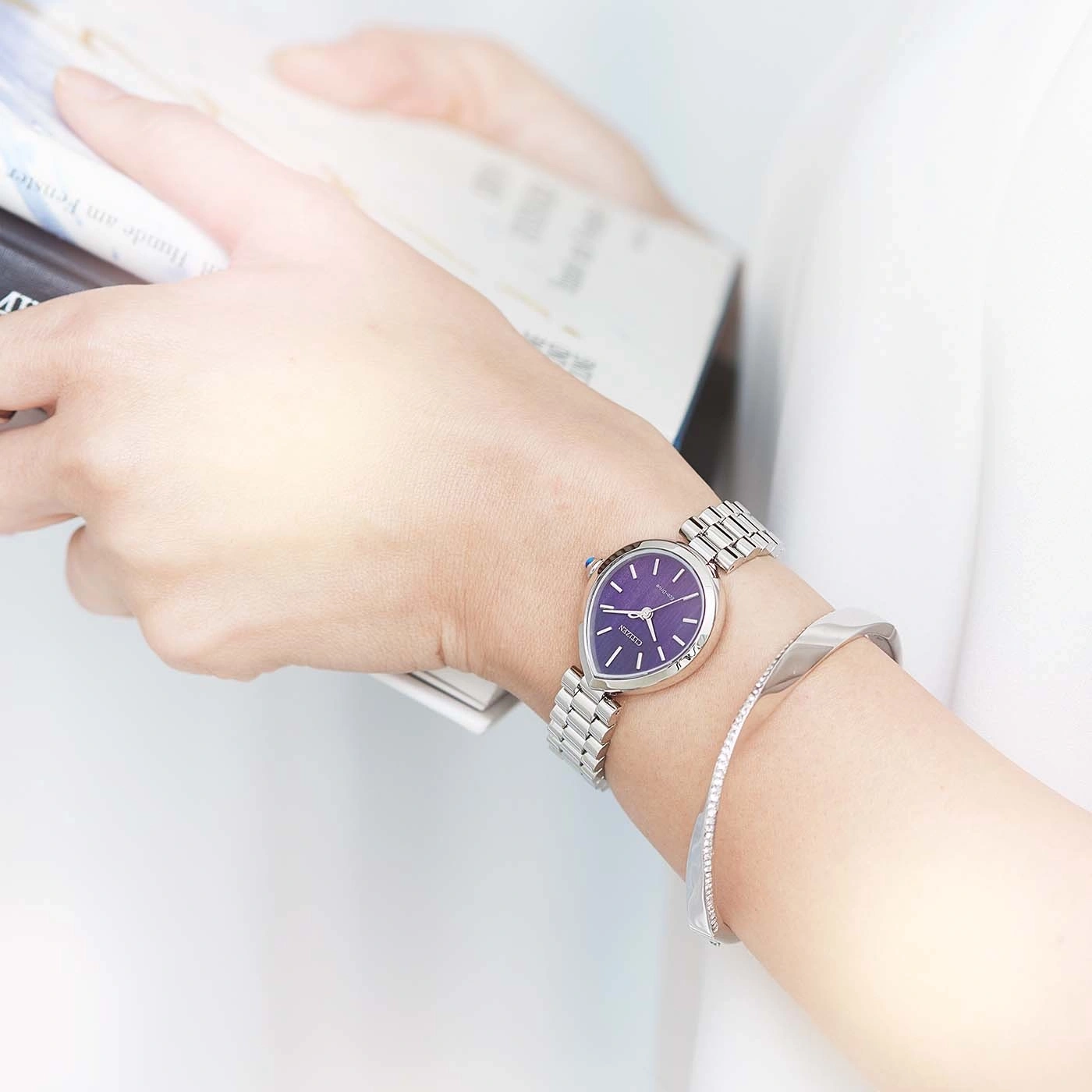 Woman wearing a purple watch and silver bracelet, reading.