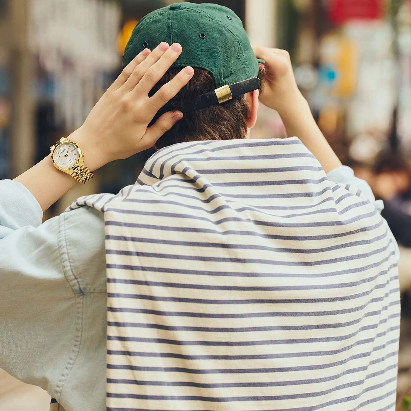 Man adjusting green baseball cap and wearing gold watch.