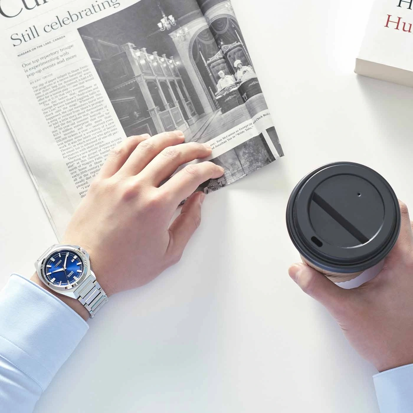 Man holding newspaper and coffee, wearing a watch.