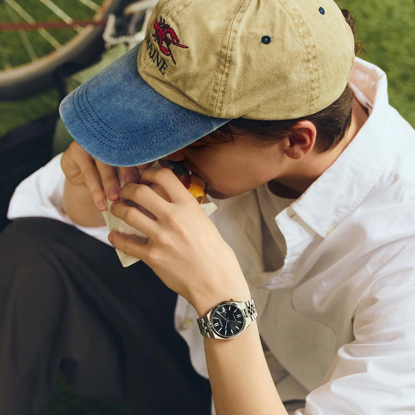 A person eating a burger wearing a baseball cap and a watch