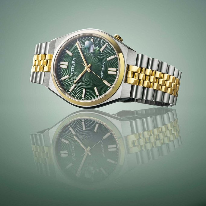 Citizen watch with green face and gold and silver band, reflected.